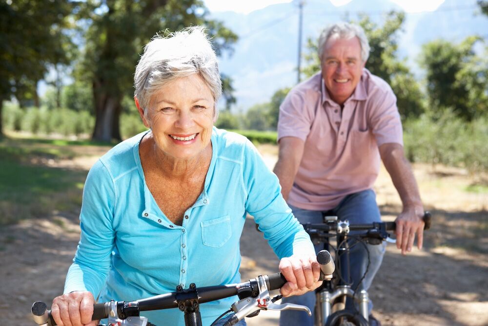A happy, healthy senior couple ride bikes around their senior living community in San Diego