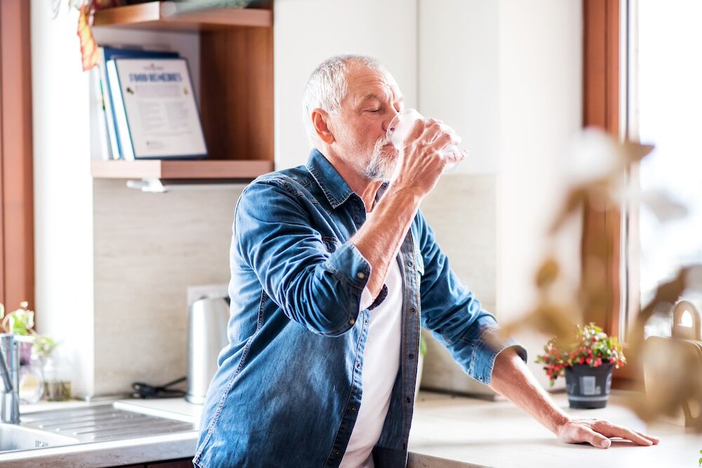 Senior man drinking water in the kitchen